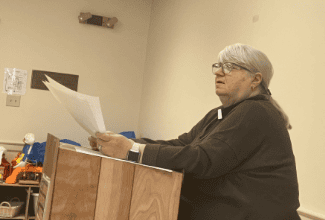 Senior woman reading papers at a podium in a church setting.